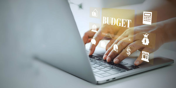 A person working on a laptop with holographic icons about budgeting appearing over their hands